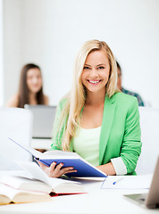 Image showing smiling young woman reading book at school