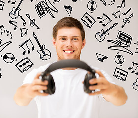 Image showing young smiling man offering headphones