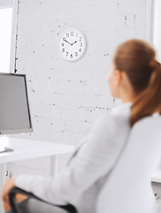 Image showing businesswoman looking at wall clock in office