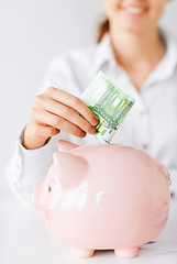 Image showing woman puts euro cash into large piggy bank