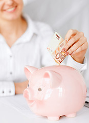 Image showing woman puts euro cash into large piggy bank