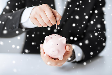 Image showing man putting coin into small piggy bank