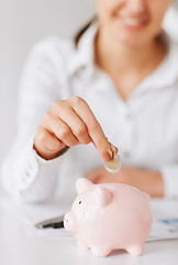 Image showing woman hand putting coin into small piggy bank