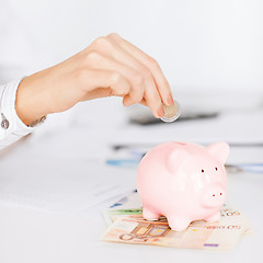 Image showing woman hand putting coin into small piggy bank