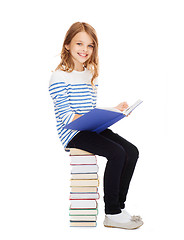 Image showing little student girl sitting on stack of books