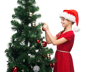 Image showing smiling girl in santa helper hat decorating a tree