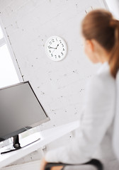 Image showing businesswoman looking at wall clock in office