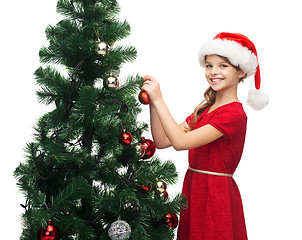 Image showing smiling girl in santa helper hat decorating a tree