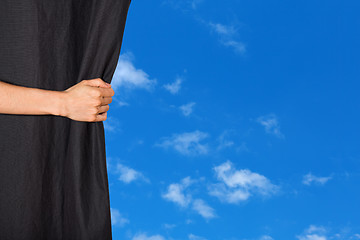 Image showing Hand opening a curtain with blue sky behind it