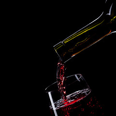 Image showing red wine pouring into wine glass isolated on black