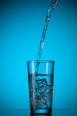 Image showing water pouring into glass on blue