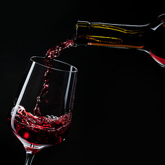 Image showing red wine pouring into wine glass isolated on black