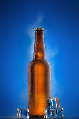 Image showing Cold beer bottle with drops, frost and vapour on blue