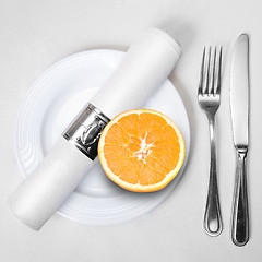 Image showing fresh orange on plate served with knife, fork and napkin