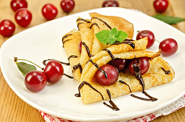 Image showing Pancakes with cherry and chocolate syrup on the board