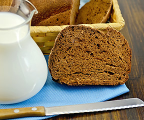 Image showing Rye homemade bread with milk and a knife on a board
