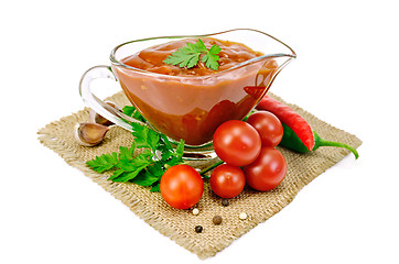 Image showing Ketchup in a glass gravy boat with vegetables on sacking