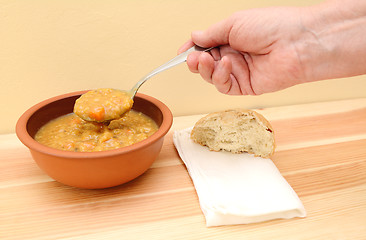 Image showing Hand holds spoonful of soup with bread roll and napkin on table