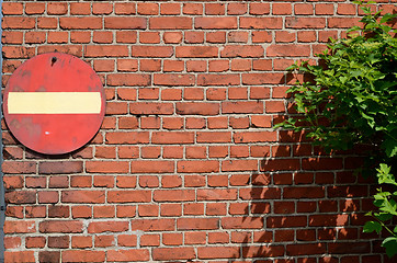 Image showing no entry road sign on a brick wall and bush