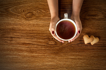 Image showing woman holding hot cup of tea with cookies on wooden table