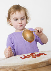 Image showing child putting sieved tomatoes on dough