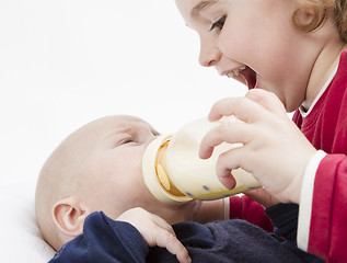 Image showing young child feeding toddler with milk bottle