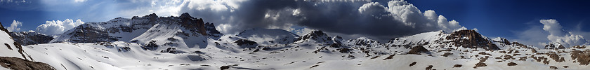 Image showing Panorama of snowy winter mountains with blue sky and dark clouds