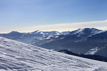 Image showing Ski slope with trace of ski, snowboards and mountains in haze