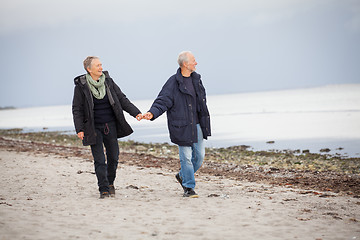 Image showing mature happy couple walking on beach in autumn