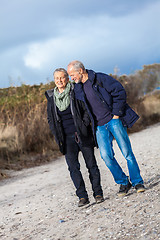 Image showing mature senior couple walking on the beach autumn winter