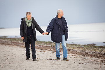 Image showing mature happy couple walking on beach in autumn