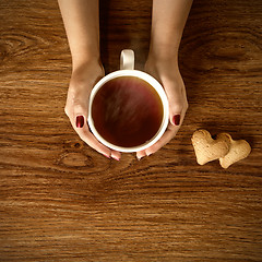 Image showing woman holding hot cup of tea with cookies on wooden table