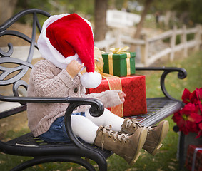 Image showing Young Child Wearing Santa Hat Sitting with Christmas Gifts Outsi