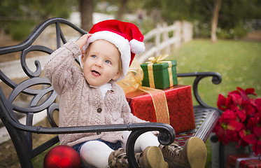 Image showing Young Child Wearing Santa Hat Sitting with Christmas Gifts Outsi