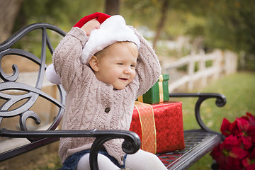 Image showing Young Child Wearing Santa Hat Sitting with Christmas Gifts Outsi