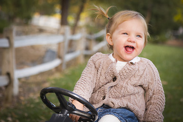 Image showing Young Toddler Laughing and Playing on Toy Tractor Outside