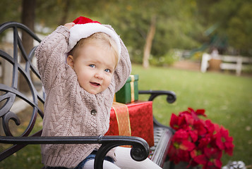 Image showing Young Child Wearing Santa Hat Sitting with Christmas Gifts Outsi