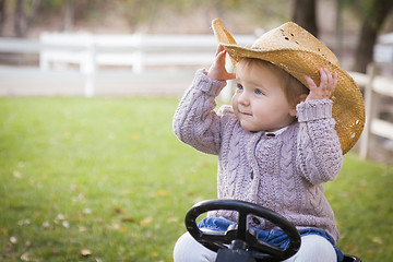 Image showing Toddler Wearing Cowboy Hat and Playing on Toy Tractor Outside