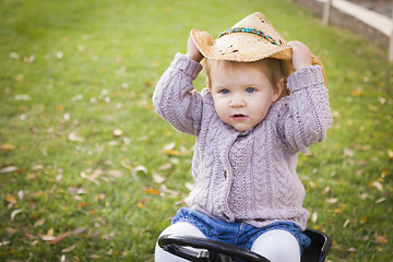 Image showing Toddler Wearing Cowboy Hat and Playing on Toy Tractor Outside