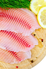 Image showing Fillets tilapia with lemon and dill on a round board