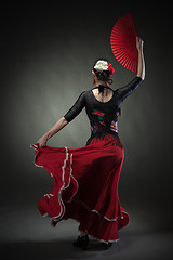 Image showing young woman dancing flamenco with fan on black