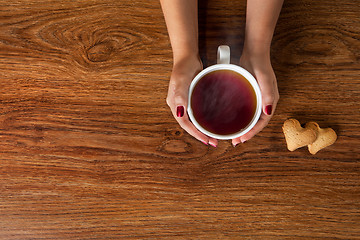 Image showing woman holding hot cup of tea with cookies on wooden table