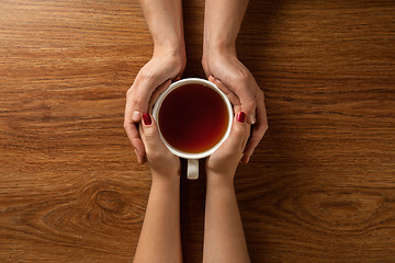 Image showing woman holding hot cup of tea with cookies on wooden table