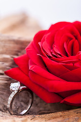 Image showing beautiful ring on wooden background and red rose