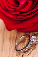 Image showing beautiful ring on wooden background and red rose