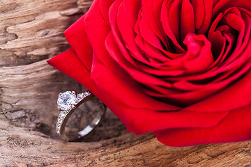 Image showing beautiful ring on wooden background and red rose