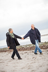 Image showing mature happy couple walking on beach in autumn