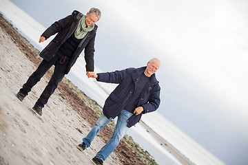 Image showing mature happy couple walking on beach in autumn