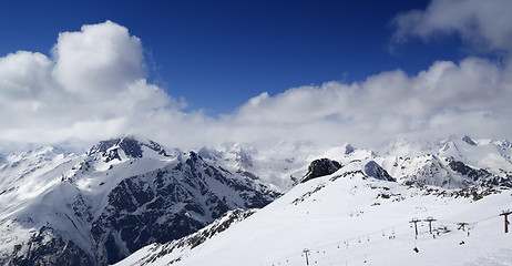 Image showing Panoramic view on ski slope and cloudy mountains at nice sun day