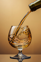 Image showing Cognac pouring from bottle into glass with splash on brown backg